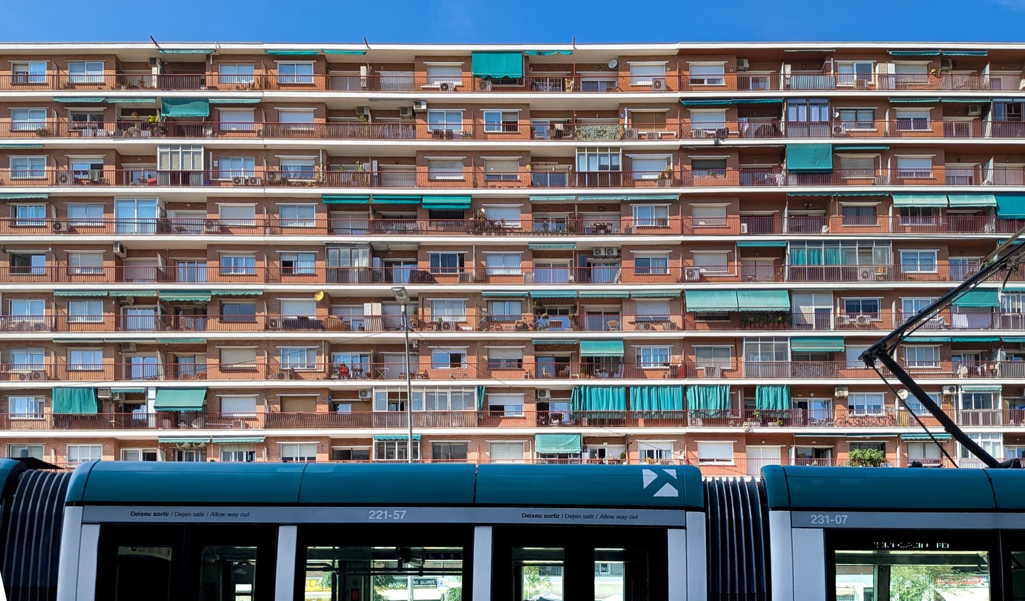 Groot appartementenblok met bewoonde balkons en groene zonneschermen, met een tram op de voorgrond